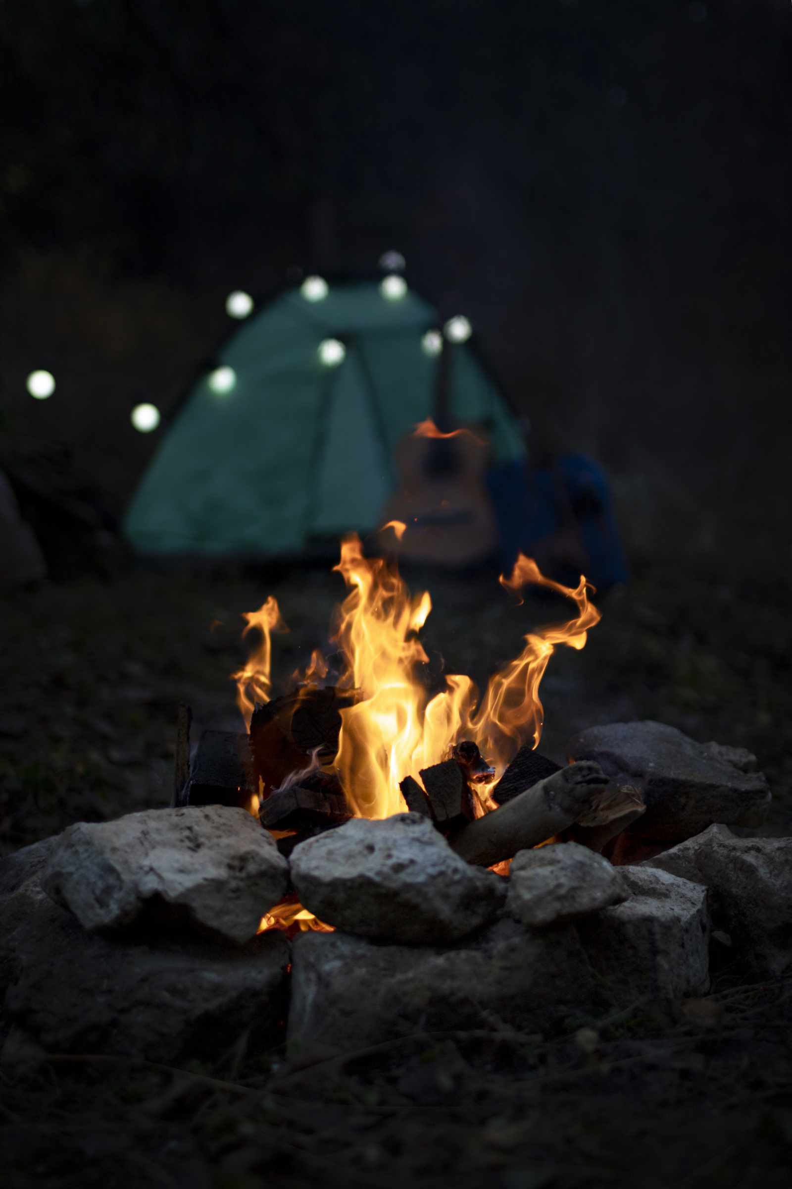 Campfire with tent and guitar in background
